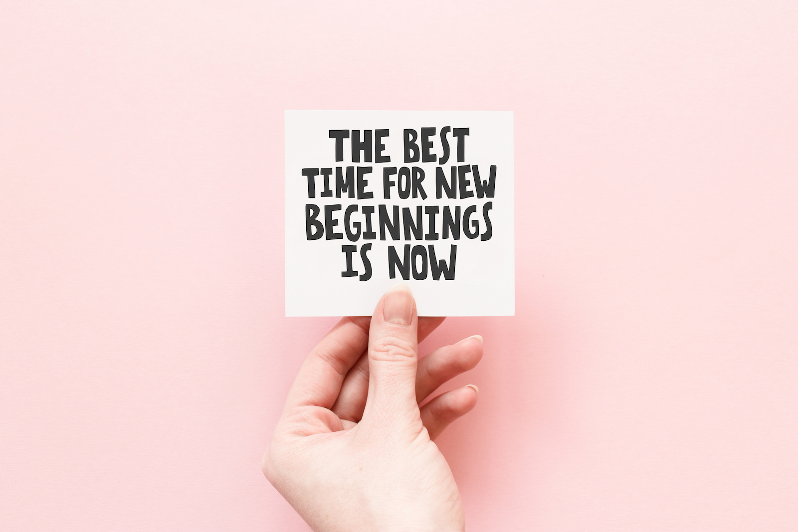 Minimal composition on a pink pastel background with girl's hand hold card with quote - The best time for new beginnings is now